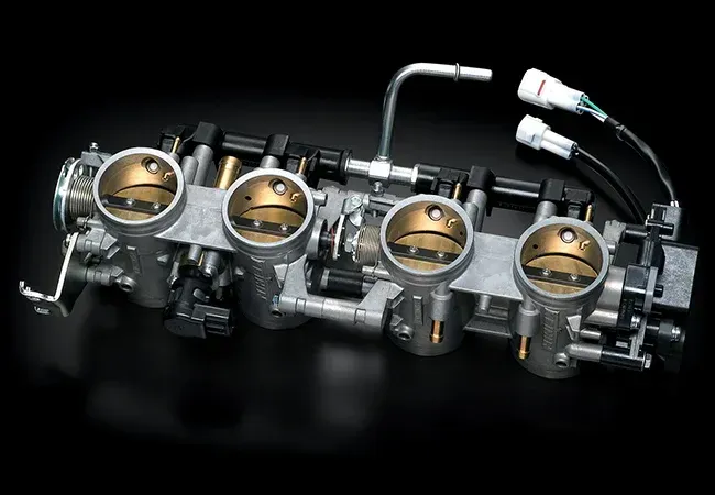 Fuel injection throttle bodies assembly. Silver metal, four throttle valves, black components, connectors, and tubing.