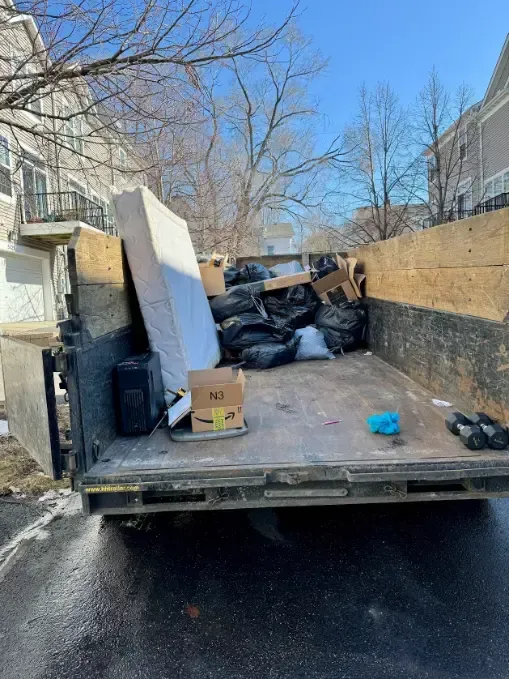 The back of a dumpster filled with trash and a mattress.