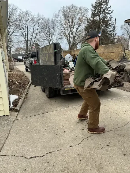 A man is carrying a pile of wood in front of a truck.