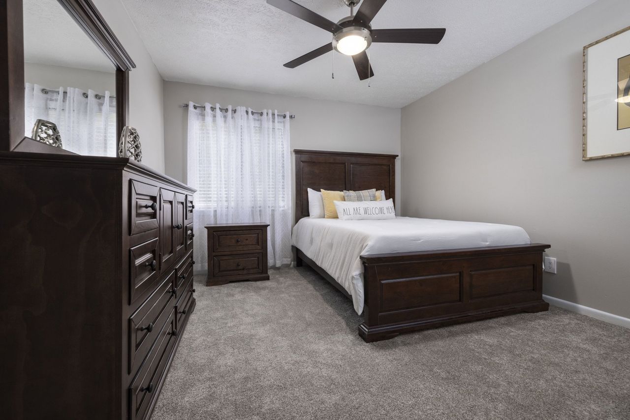 A bedroom with a bed , dresser , mirror and ceiling fan at Cross Creek.