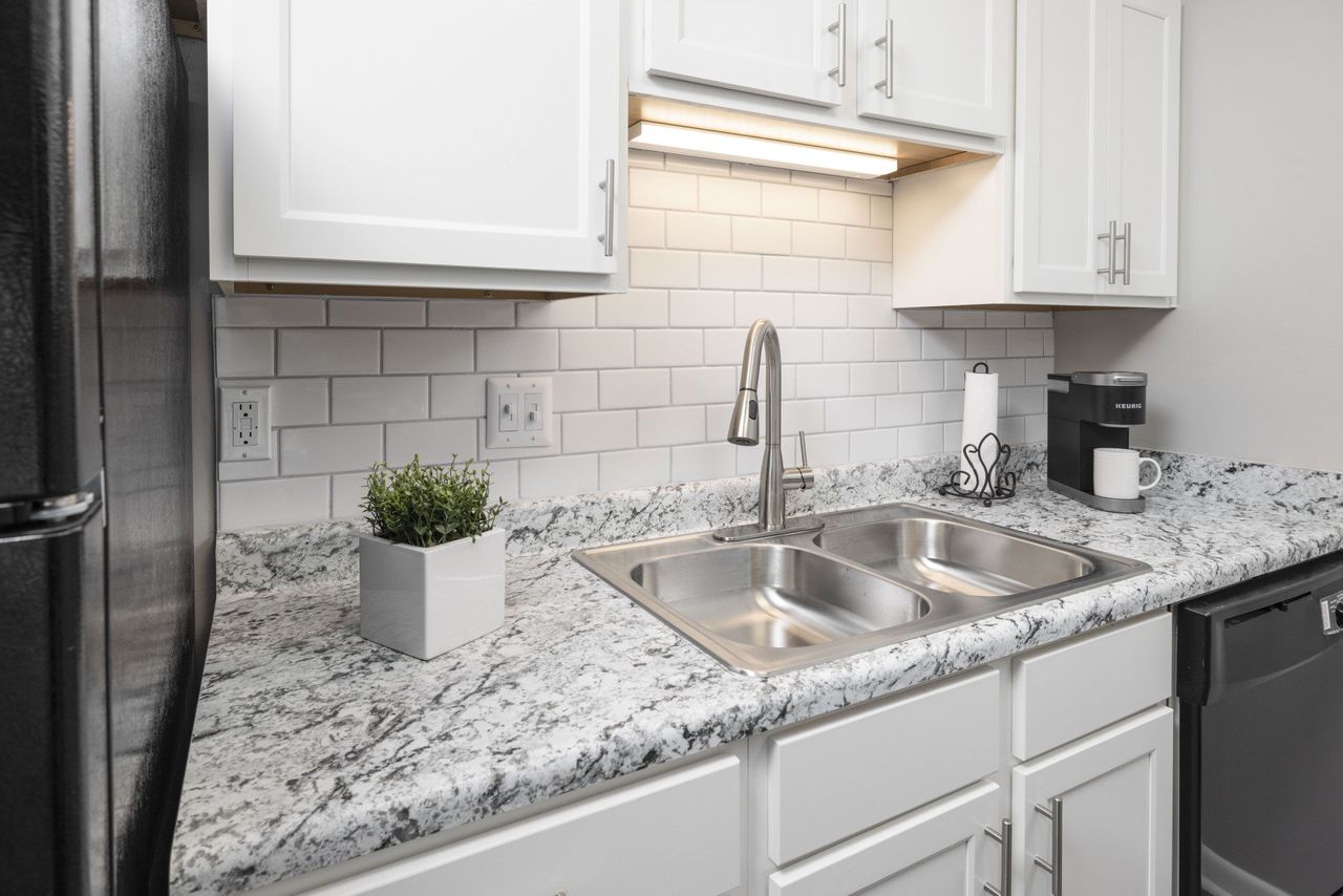A kitchen with white cabinets , granite counter tops , a sink and a refrigerator at Cross Creek.