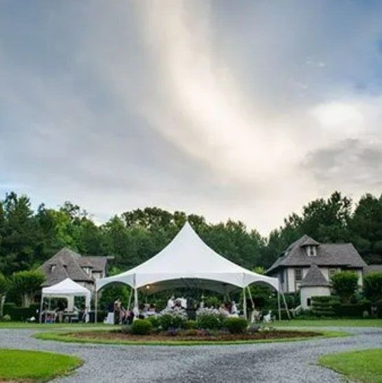 A large white tent is sitting in the middle of a grassy field in front of a house.