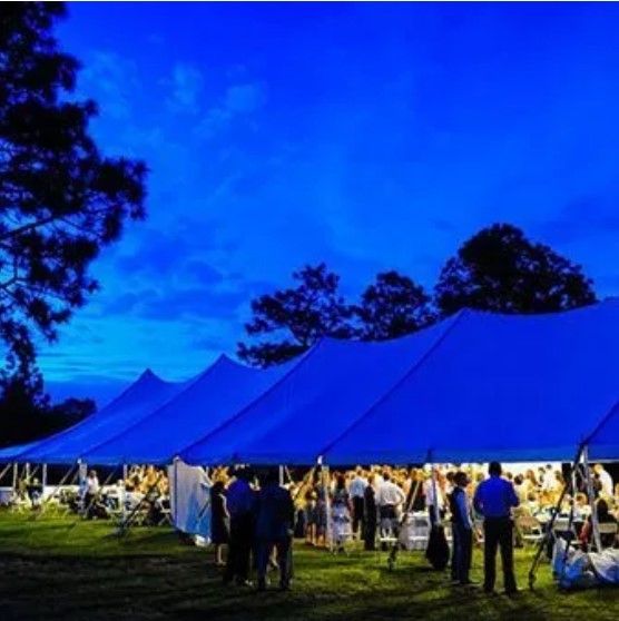 A group of people are standing under a blue tent at night.