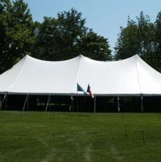 A large white tent is in the middle of a grassy field