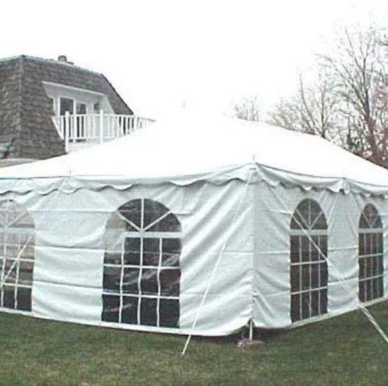 A white tent with arched windows is sitting in the grass in front of a house.