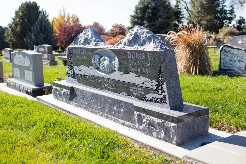Wide view of the Burgess family headstone featuring dual panels, carved designs, and a landscaped cemetery setting with surrounding graves.