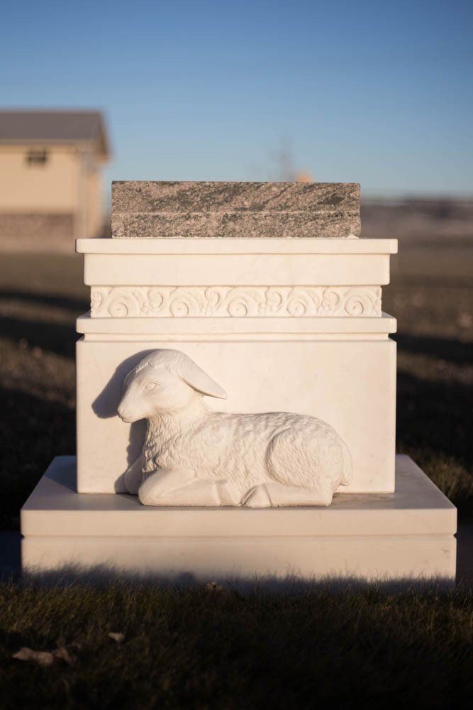 Stone sculpture-style memorial with carved lamb resting on top of rectangular base