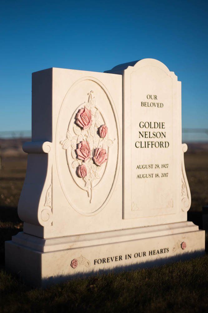 Beige upright headstone for Goldie Nelson Clifford featuring carved roses and gentle border design