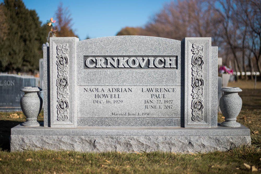 Gray granite companion headstone for Nava and Lorraine Crnkovich with religious and floral carvings