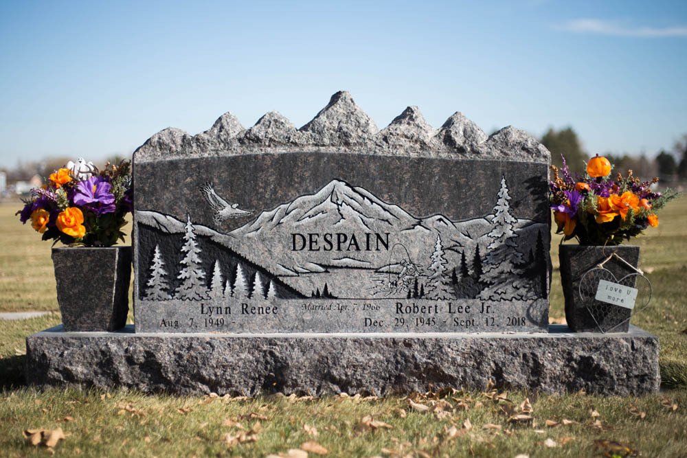 Forest-etched granite double headstone for the Despain family with colorful flower arrangements