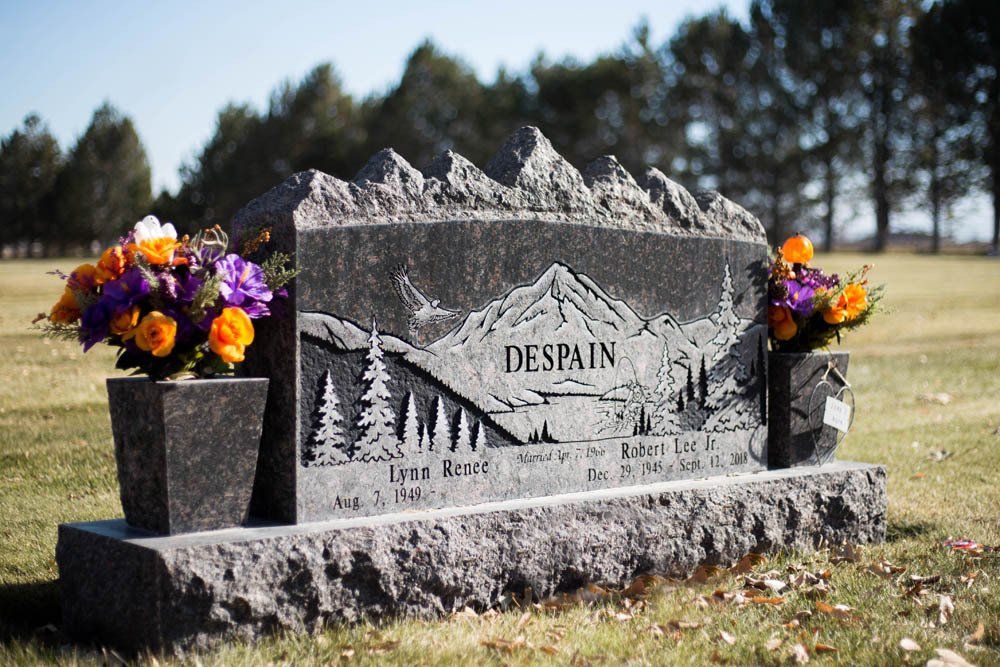 Side angle of Despain family memorial with carved trees and mountains on dark granite