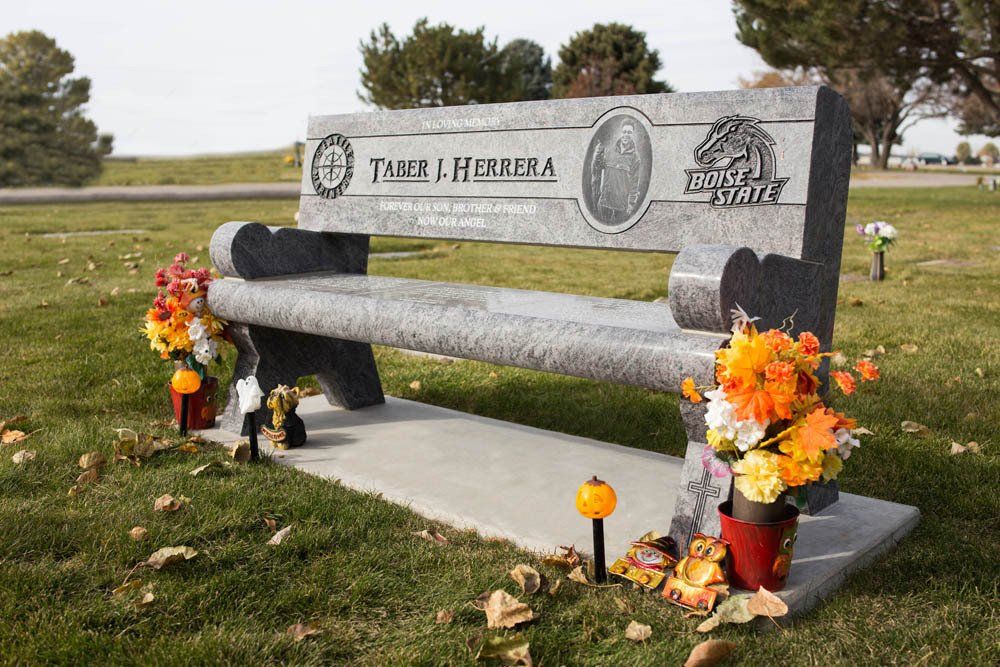 Angled view of Herrera memorial bench with flower arrangements and forest engraving on backrest