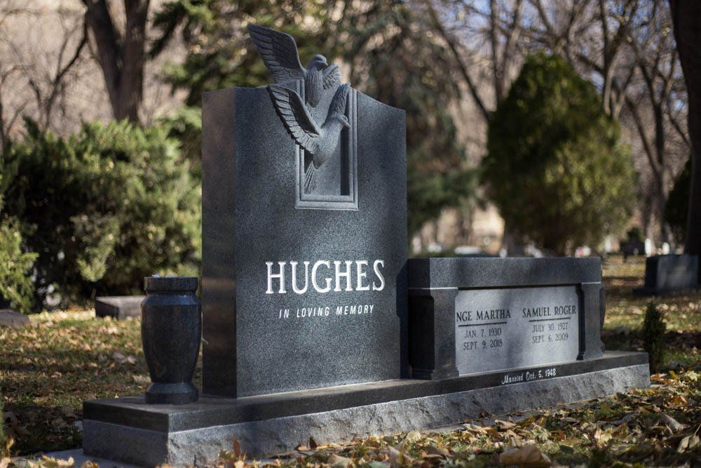 Side view of Hughes headstone showing upright centerpiece with trees and companion plaques at base