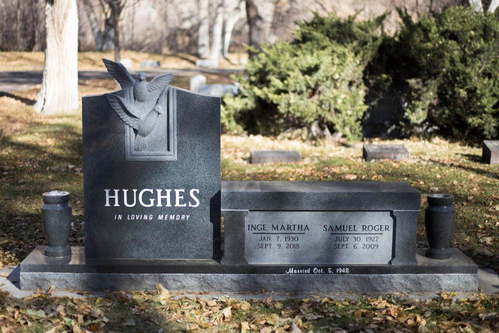 Double upright granite headstone for Hughes family with engraved trees and inset plaques