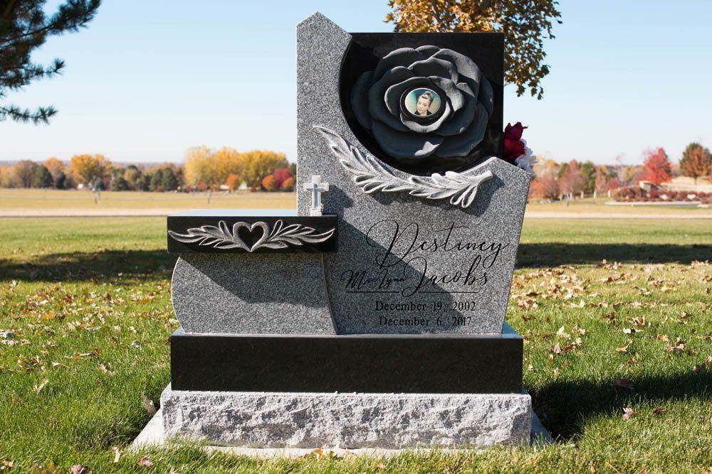 Sculpted angel-themed headstone with rose carving and engraved dedication to “Jacobs”