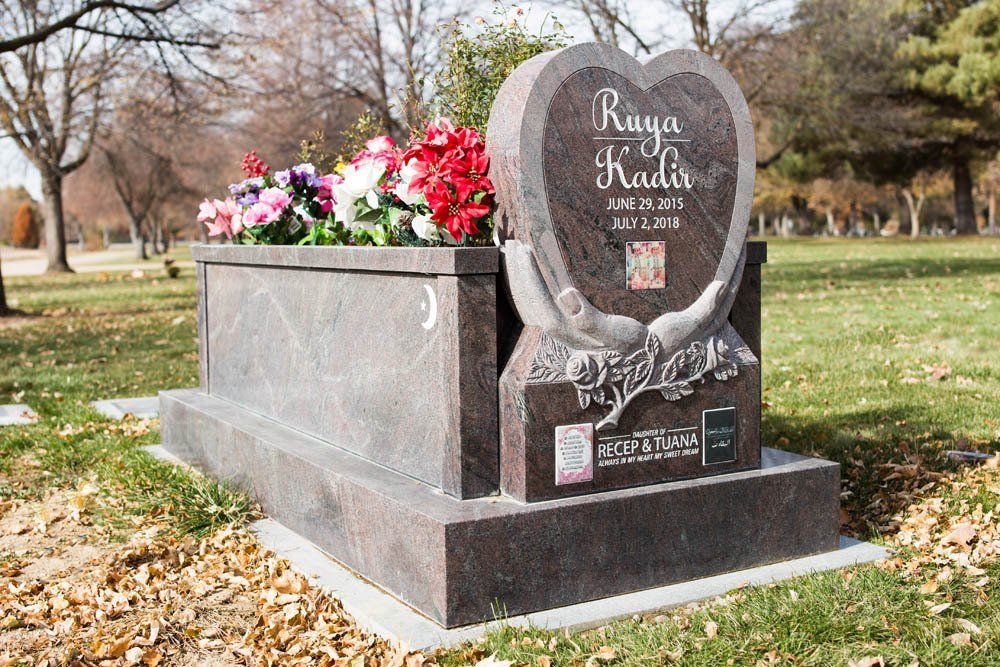 Red granite child memorial for Ruya Kadir with engraved hands holding a heart and colorful flowers