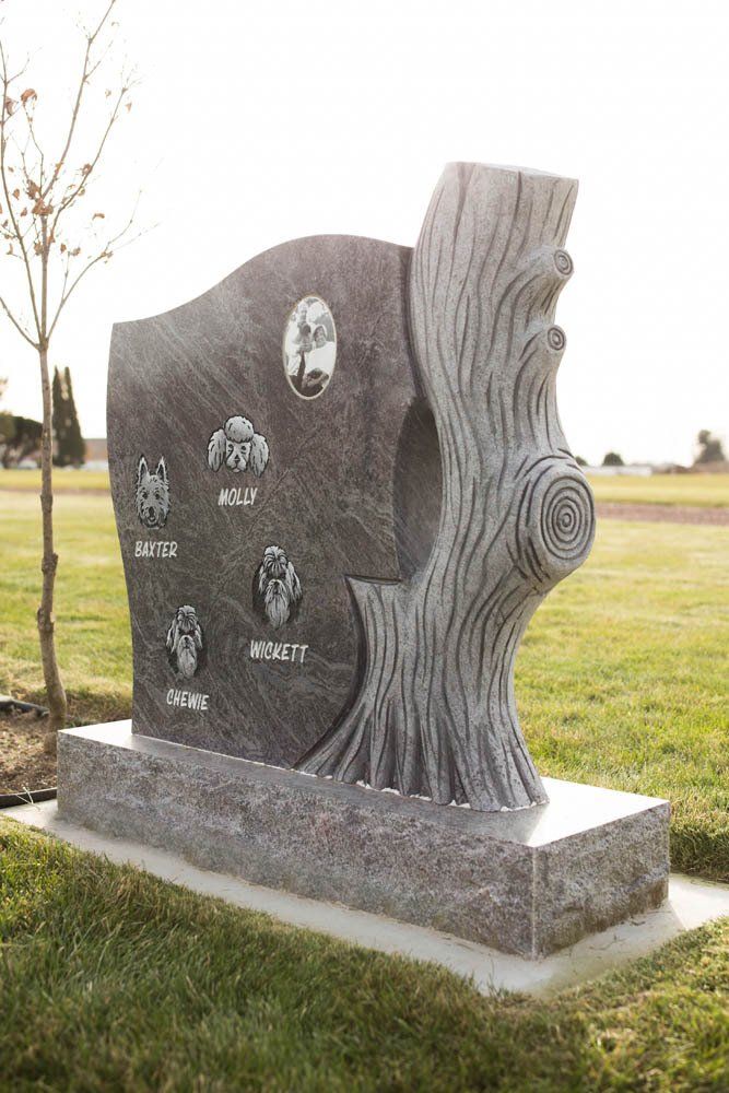 Side view of granite pet headstone with carved tree trunk design and pet name engravings