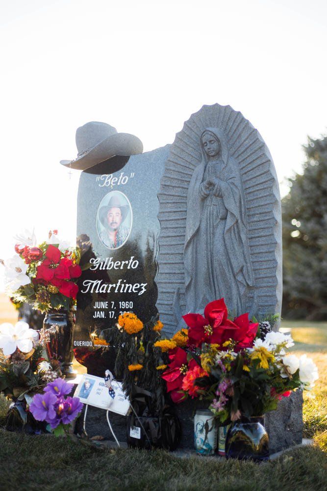 Front-facing monument for Gilberto Martinez with Catholic iconography and colorful floral arrangements