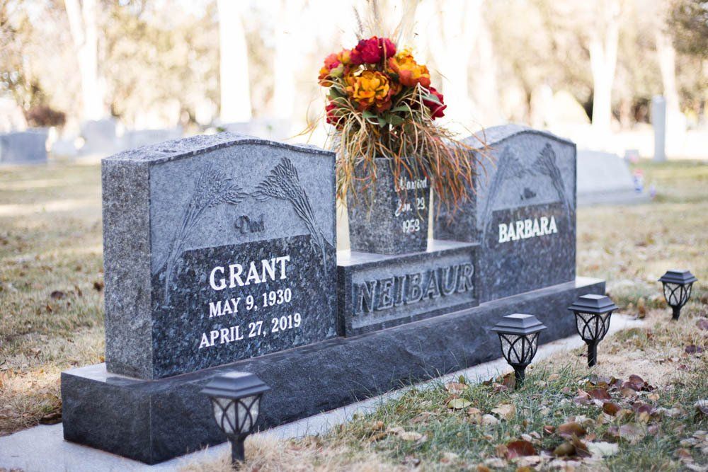 Three-part granite headstone for Grant and Barbara Neibaur with engraved wheat design and floral arrangement