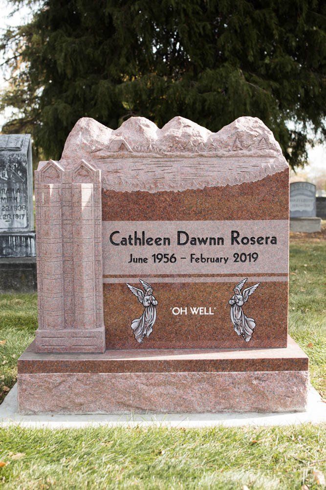 Red granite monument for Cathleen Dawn Rosera with angel illustrations and the inscription “Oh Well”