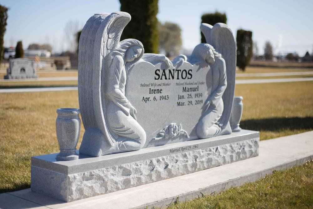 Granite headstone for Irene and Manuel Santos featuring two kneeling angel sculptures and floral base