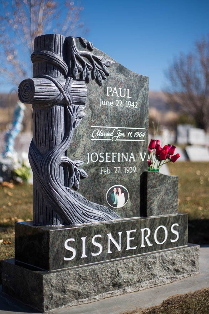 Side view of dark green granite headstone with sculpted cross and red roses for Josefina V.