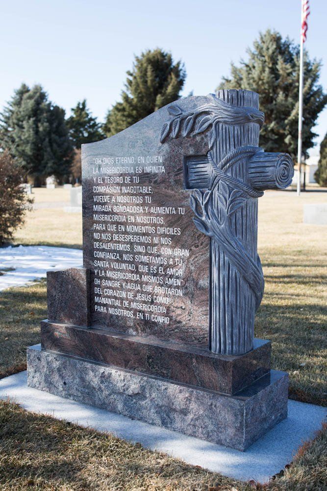 Spanish-inscribed granite headstone with raised cross and praying hands sculpture in a cemetery