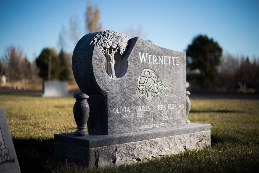 Side view of custom Wernette headstone with carved truck and tree detailing in cemetery