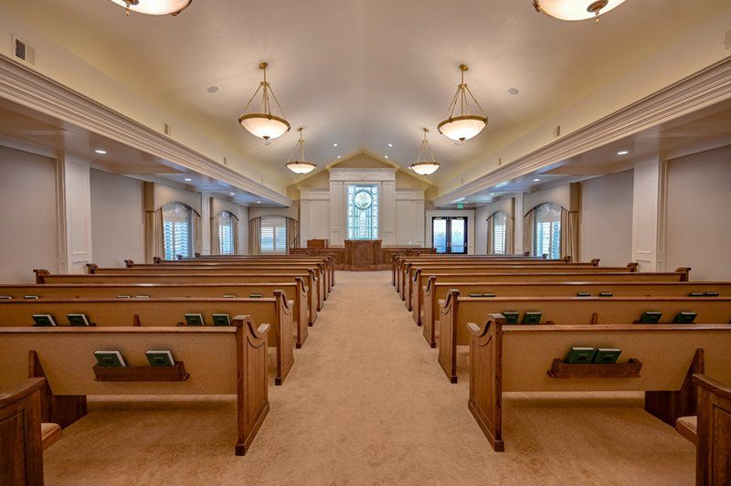 The white pine funeral services chapel showing several bench rows of seating and hymn books with warm lighting and clean carpet.