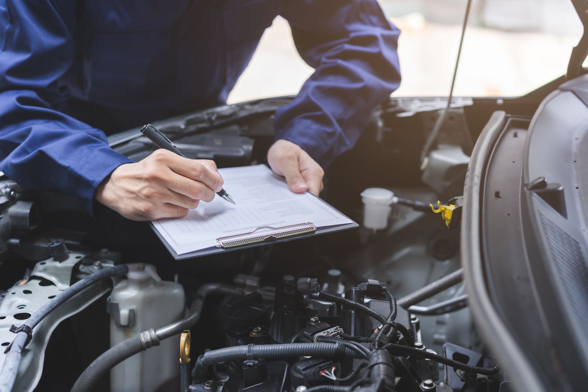 A mechanic is writing on a clipboard while working on a car.