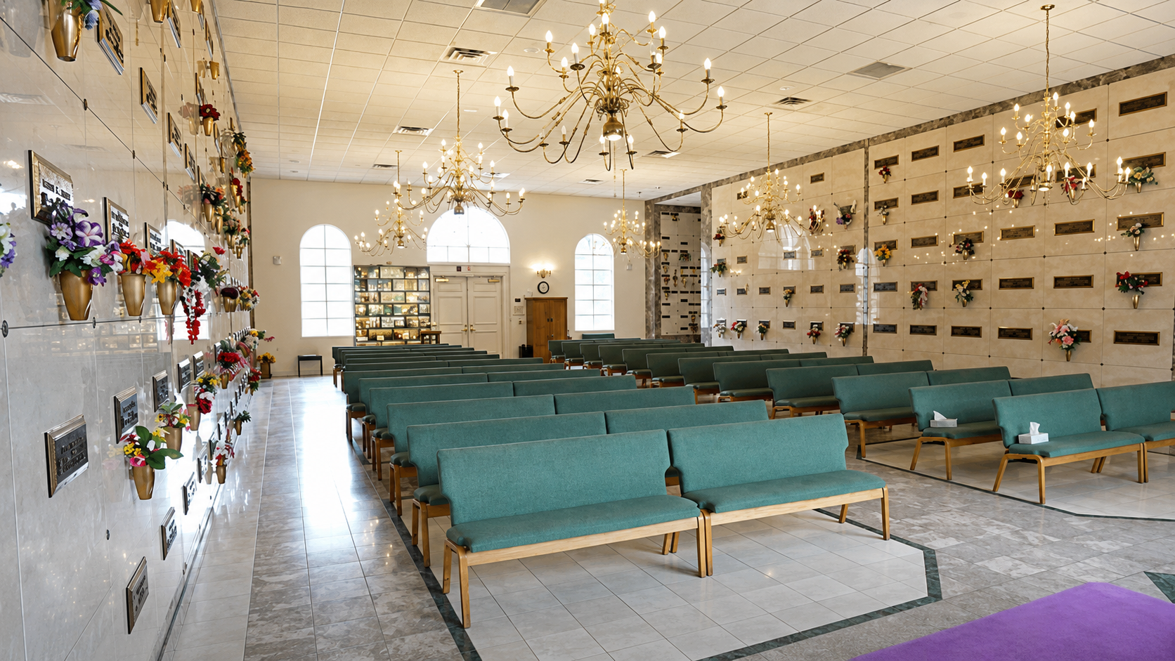 Bright memorial hall with green benches, chandeliers, and wall niches for urns or plaques