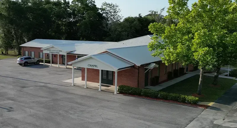 Low brick office building with metal roofs, front awning, and empty parking lot surrounded by trees