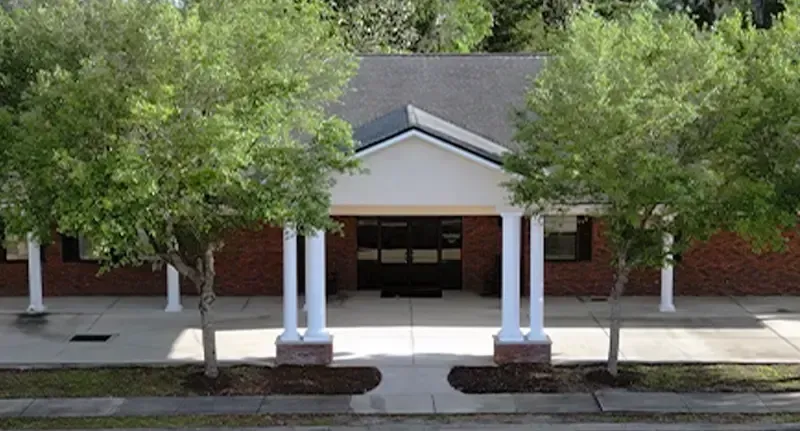 Front entrance of a brick building with white columns and trees lining the walkway