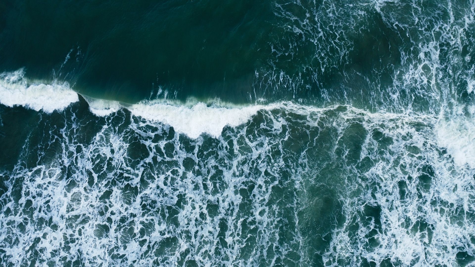 Aerial view of dark blue ocean waves crashing into white foam