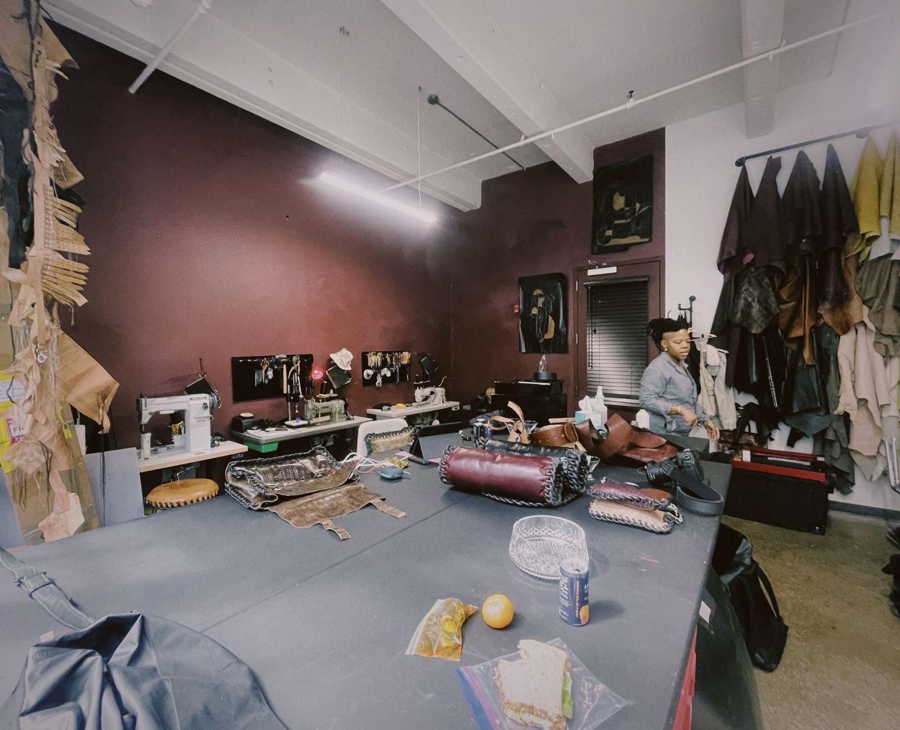 A woman in a leather workshop with a sewing machine and a lot of leather draped on the wall
