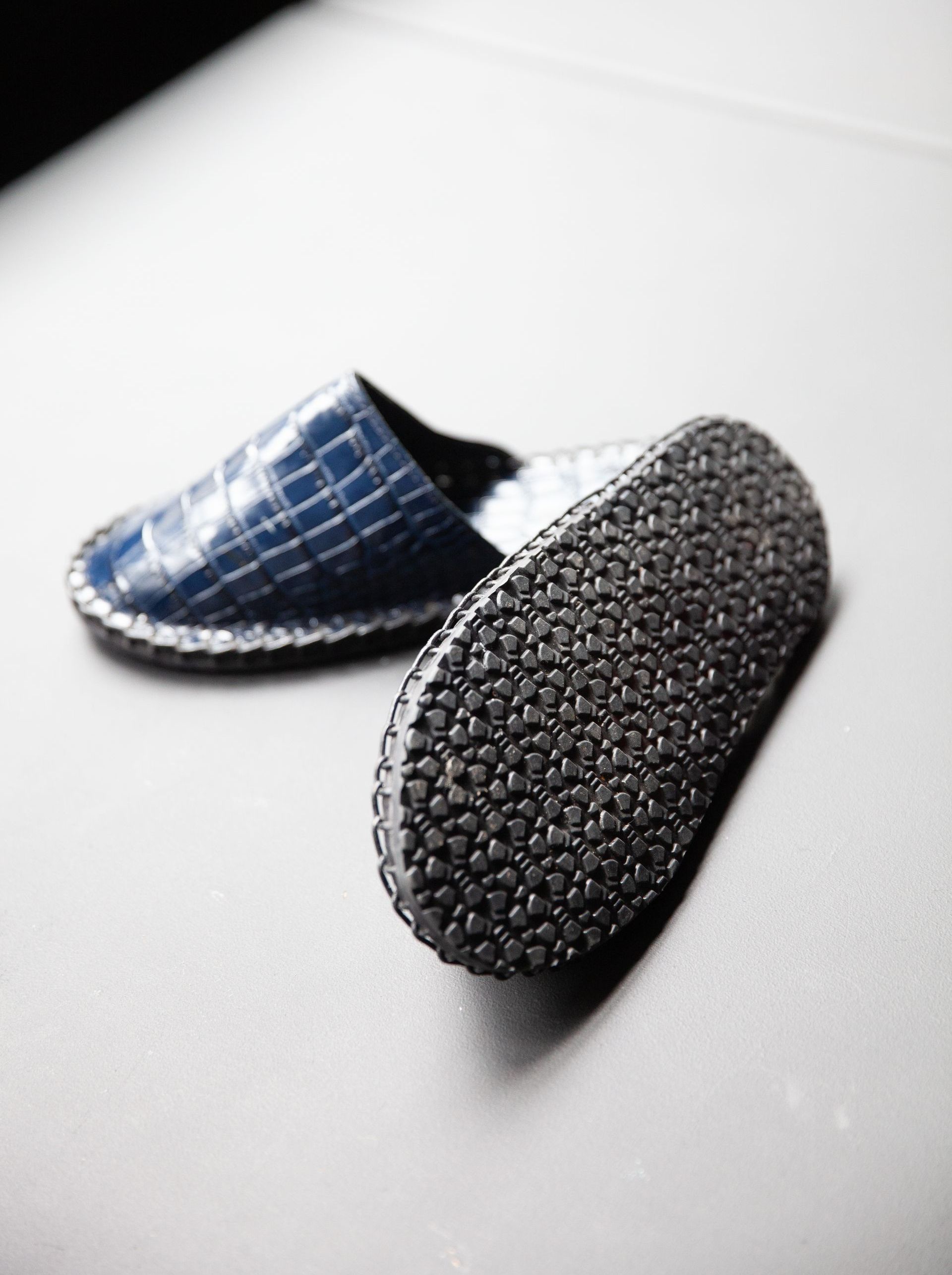A pair of blue slippers with a black sole on a white surface.