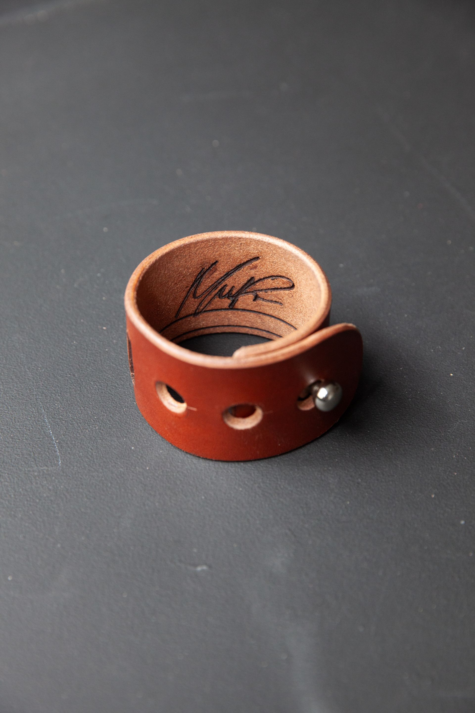 A brown leather ring is sitting on a black surface.