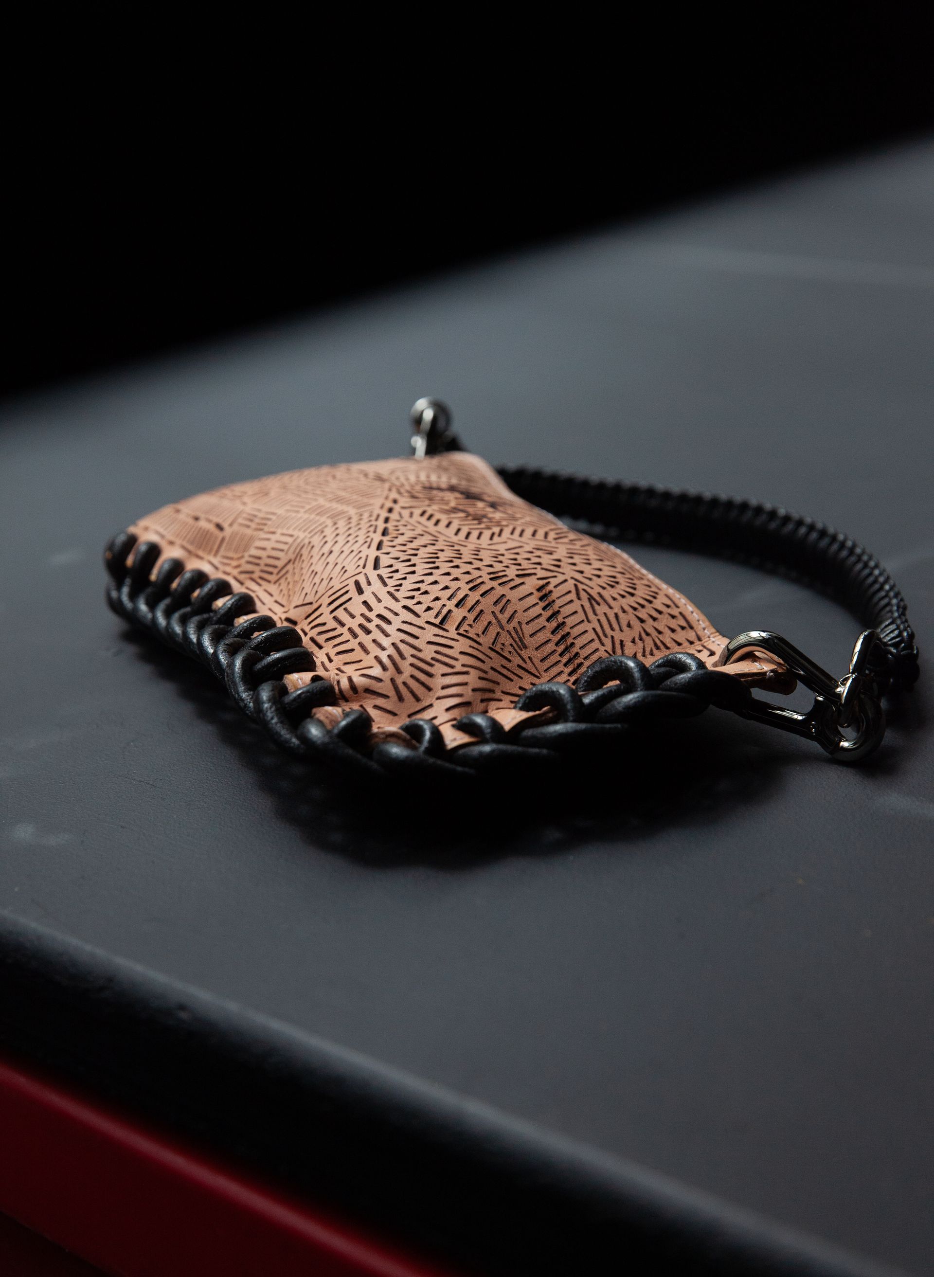 A brown leather purse with a black chain is sitting on a black surface.