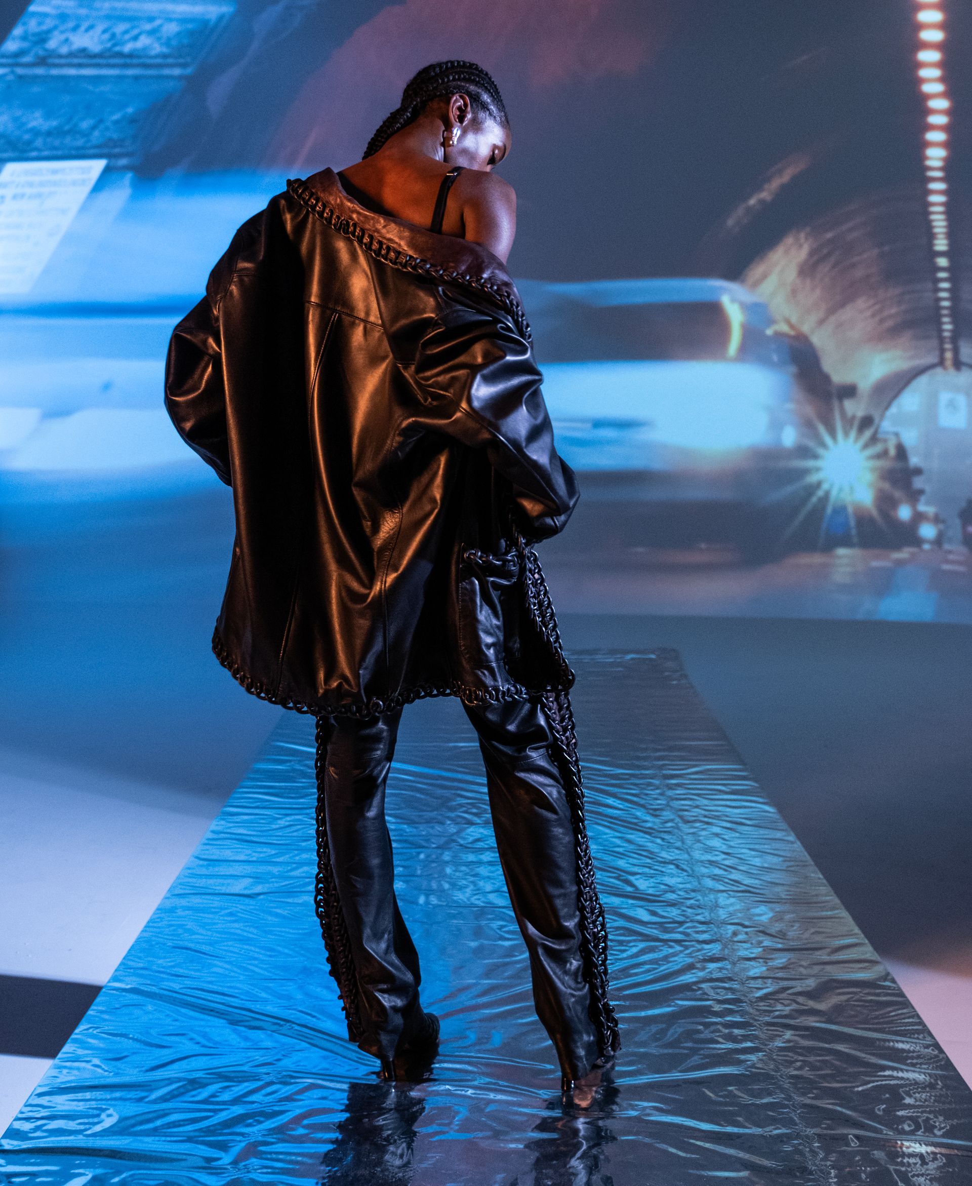 A man in a black leather jacket and pants is standing on a runway.