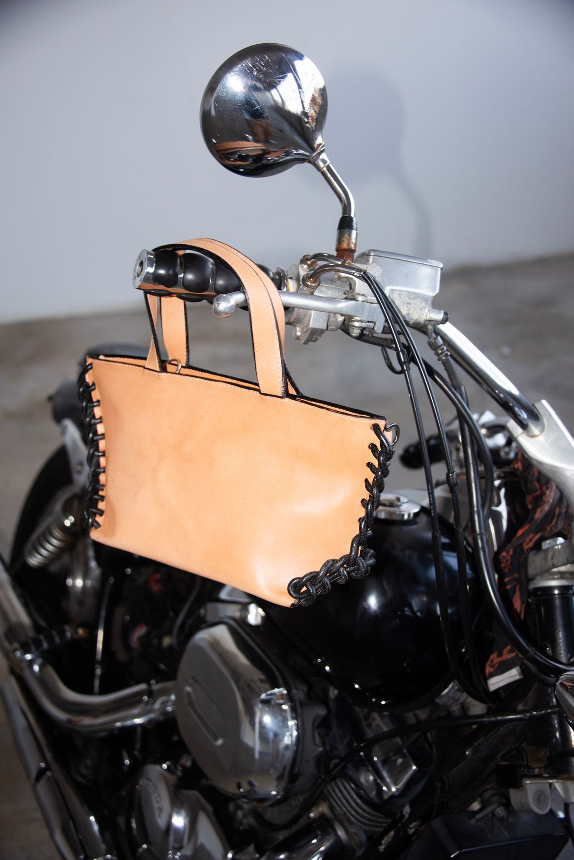 A brown leather bag is hanging from the handlebars of a motorcycle.