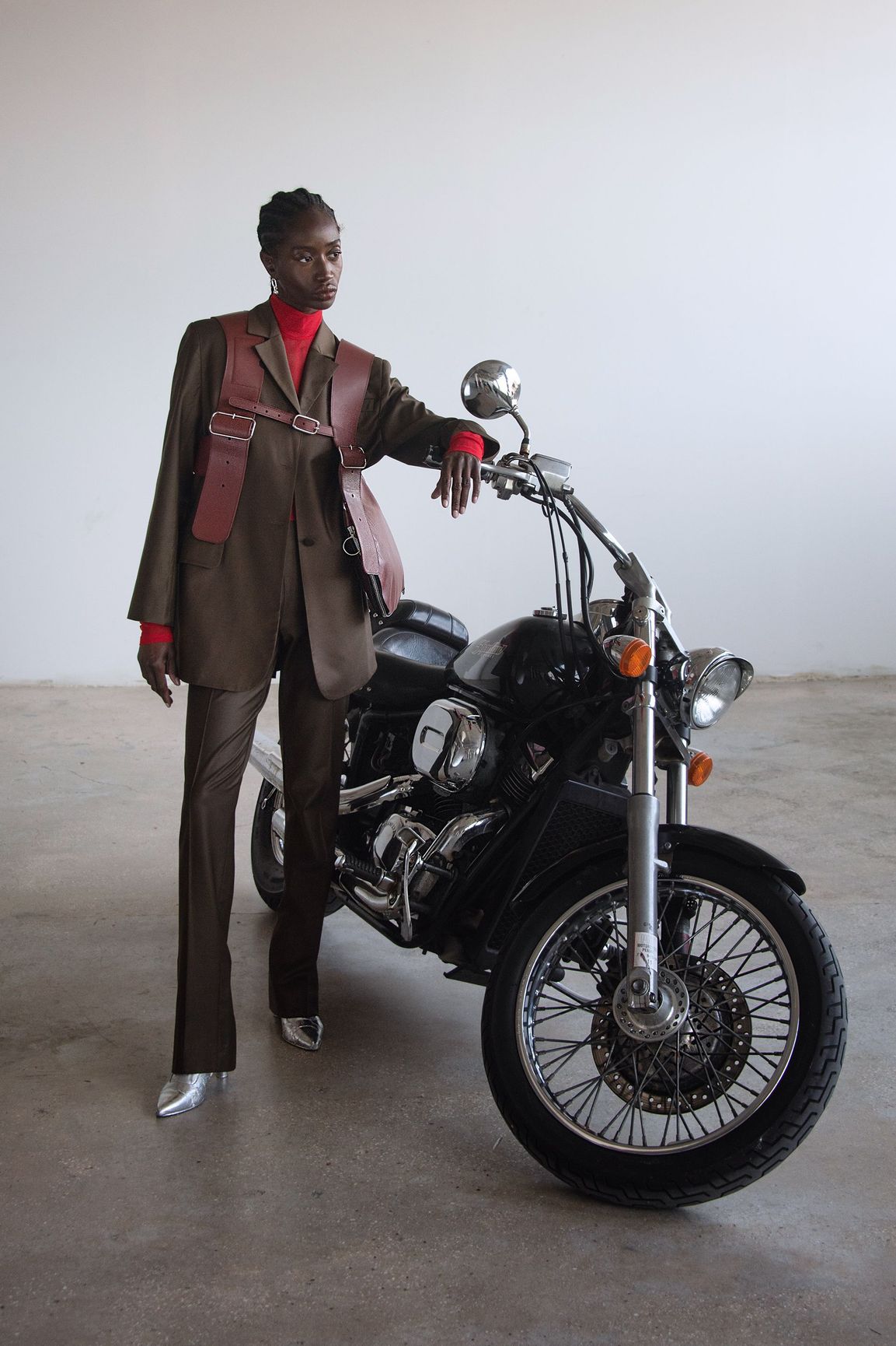 A woman in a suit is standing next to a motorcycle.