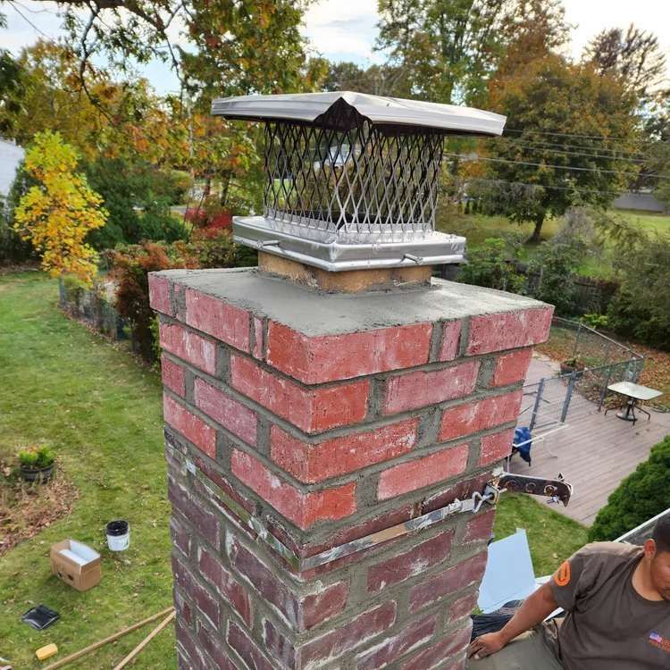 Brick chimney with cap; person in orange shirt working on the roof.