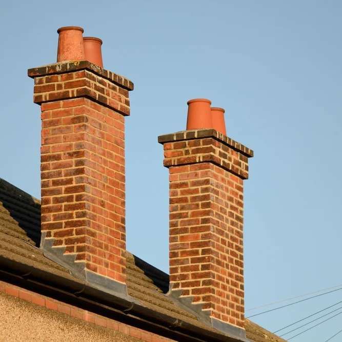 Two red brick chimneys with terracotta chimney pots, against a blue sky.