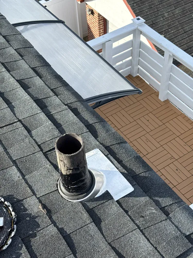 Chimney on a shingled roof next to a small deck with white railing.