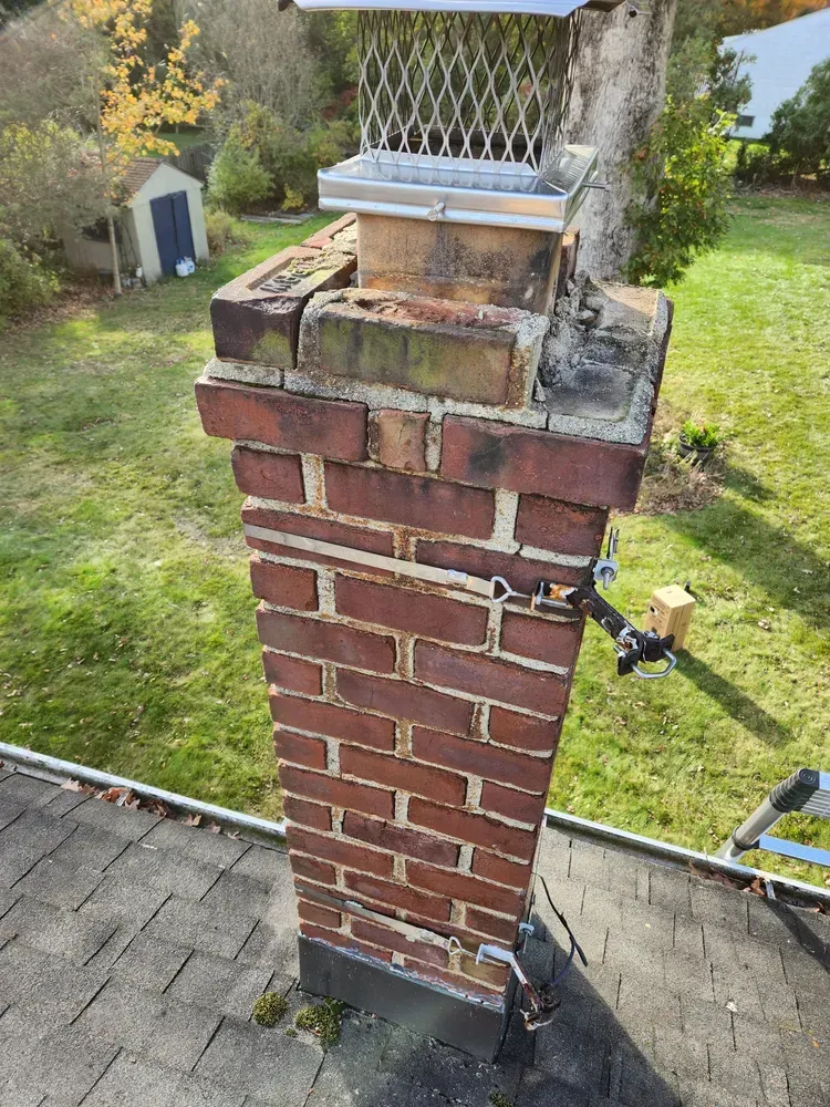 Brick chimney with metal cap on a rooftop, viewed from a slightly elevated angle.