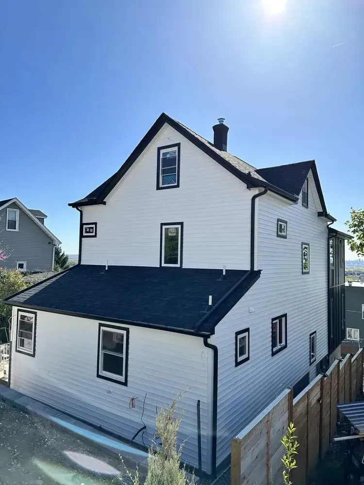 White two-story house with black trim, windows, and roof against a blue sky.