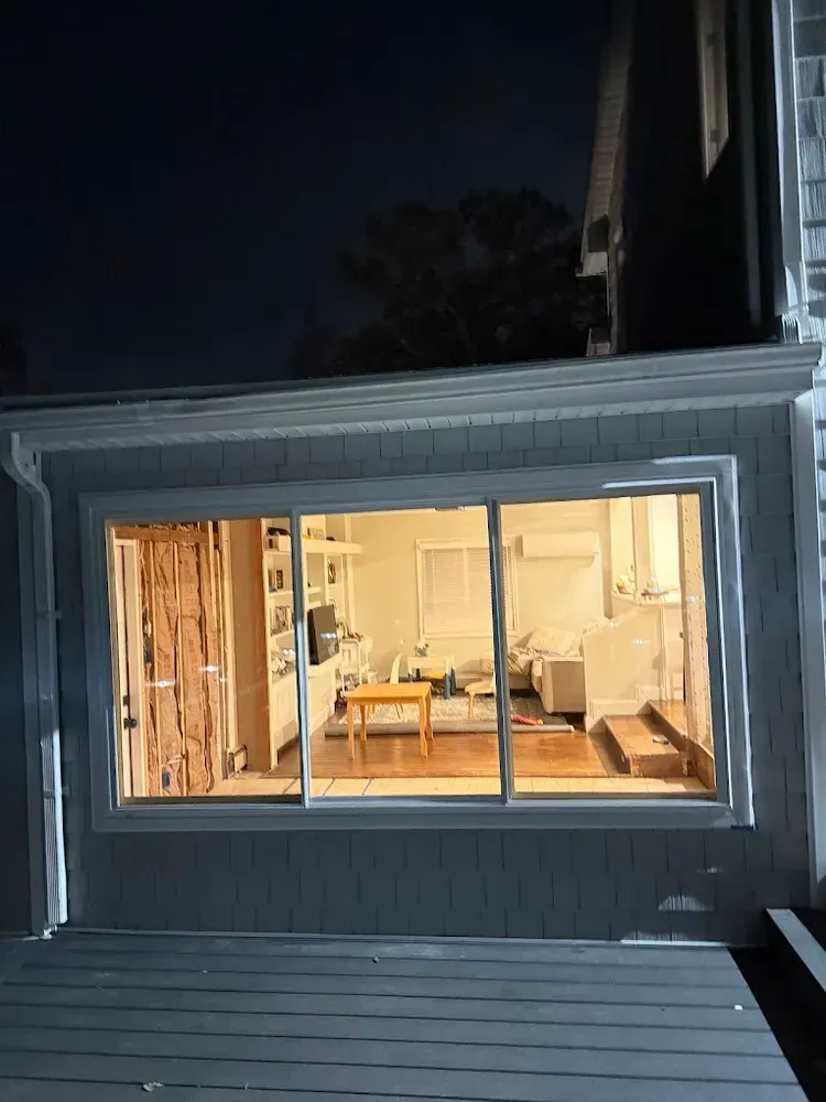 Exterior night view of a brightly lit kitchen visible through a large window.