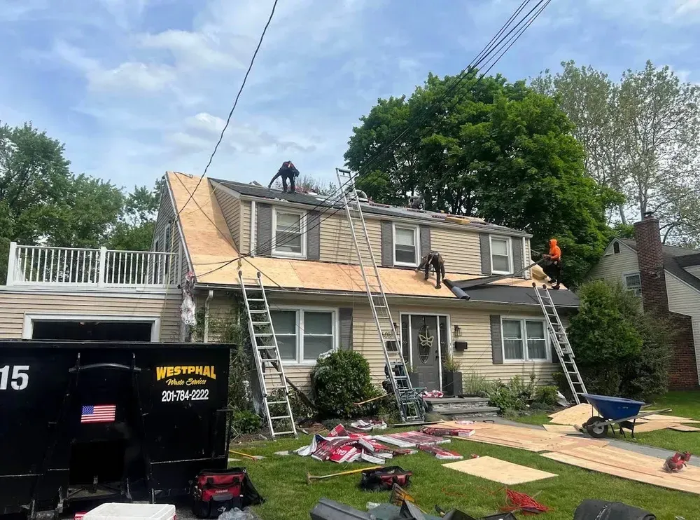 Roofers working on a house, with ladders and a dumpster on the lawn.