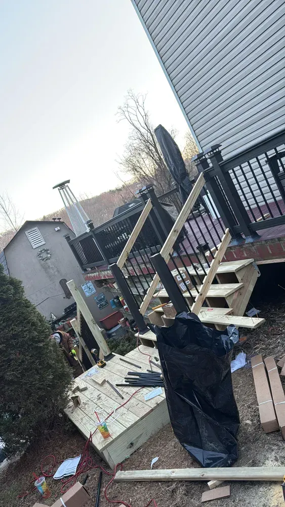 Construction site with a partially built deck and stairs, debris, and a house.