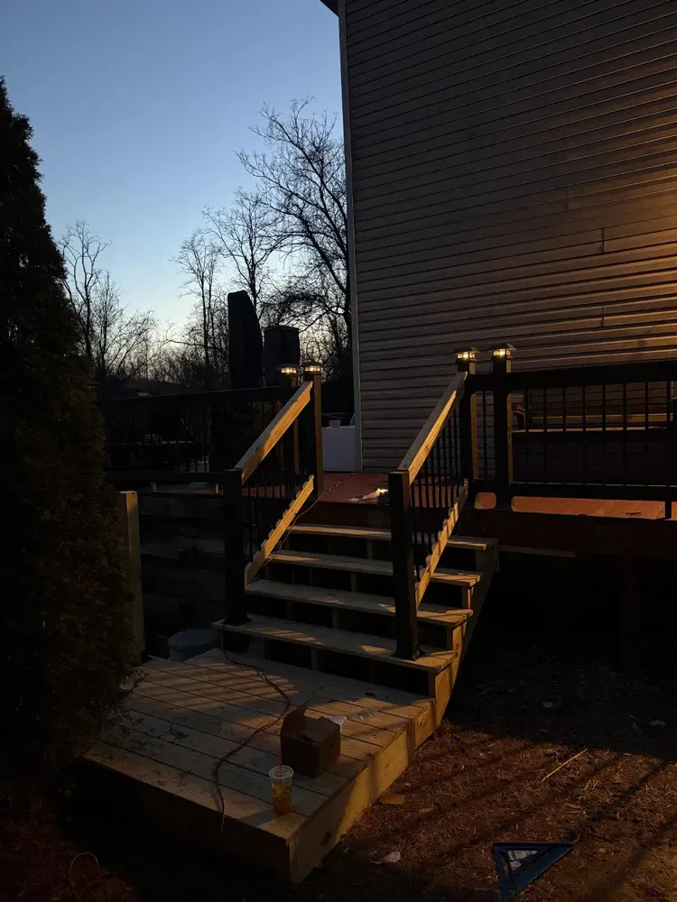 Outdoor staircase leading up to a deck, against a house at dusk.